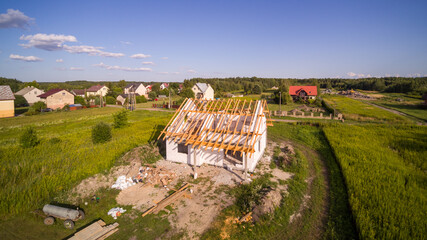 Aerial view on detached house under construction. House Ii basic state. Located on green plot in small village. Wooden roof structure. Meadows around.