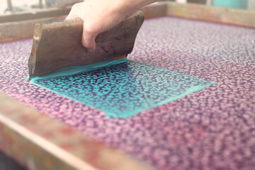 A screen printing squeegee is guided by hand over a large silk-screen to print a detailed clover...