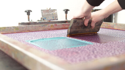 A detailed design is printed by hand with a squeegee and large silk-screen in different colors for sampeling - handicraft and exclusive fashion concept - background blanked out blurry