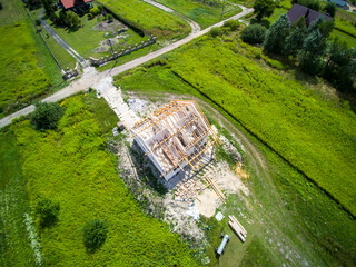 Top-down view on detached house under construction. House in basic state. Located on green plot in small village. Wooden roof structure. Meadows around.