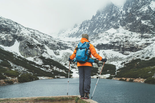 Active people in nature concept. Dressed bright orange jacket female backpacker enjoying the Velicke pleso (mountain lake) view as she have mountain walk in Velicka valley in High Tatras, Slovakia.
