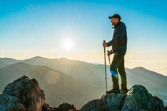 Hiker Man standing with trekking poles on a cliff edge and looking at Tatra mountains valley covered with clouds. Successful Velky Rozsutec 1610m summit and success concept image.