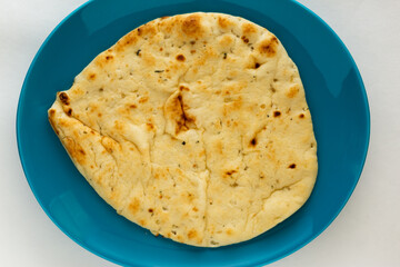 Authentic naan flatbread seasoned with roasted garlic placed on teal porcelain plate on white background