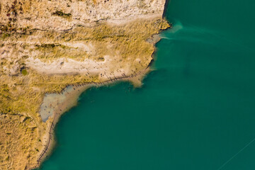 Luftaufnahme von einem Uferbereich von einem See an dem sich Sand und Vögel wie Enten tummeln