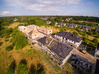 Aerial view on settlement of detached houses under construction. House in basic state. Located on green plot in small village. Wooden roof structure. Meadows around.