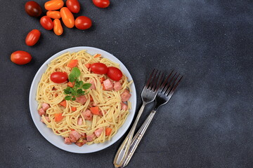 Italian spaghetti pasta with cherry tomatoes, tomato sauce, basil, fried carrots and sausage on a dark table, top view, place for text, selective focus