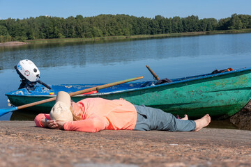 Tourist woman lying on a rock on the shore of the lake next to the boat