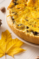 Quiche pie with mushrooms and cheese, autumn background with fallen maple and oak leaves, pine cones and hazelnuts