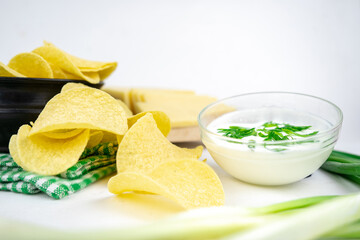 Take a chips from a bowl and dip it in a sour cream sauce with green onion.