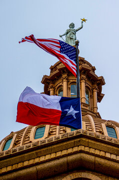 American and Texas State flag flying in front of the dome of the state house capital building in Austin.