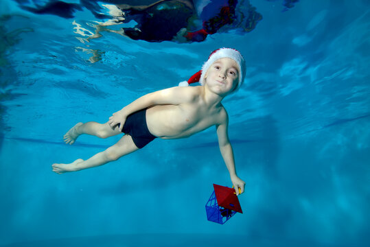 Funny child, boy, swims underwater in the pool in a red Santa hat with a toy in his hand. Portrait. Concept. Horizontal orientation of the photo