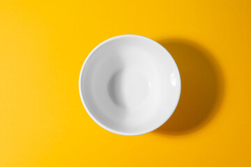 Top view on a white deep bowl on yellow background.