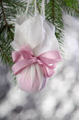 Christmas ball wrapped in a medical mask with a pink ribbon.