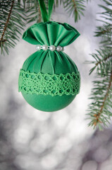 Green Christmas ball with a pattern on a spruce branch on a silver background.
