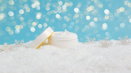 Opened face cream jar and snowflakes in snow on blue background with bokeh lights. Moisturizing...