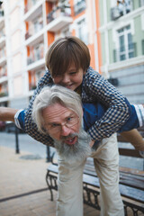 Vertical shot of a cute young boy having fun with grandpa, piggyback riding on city streets