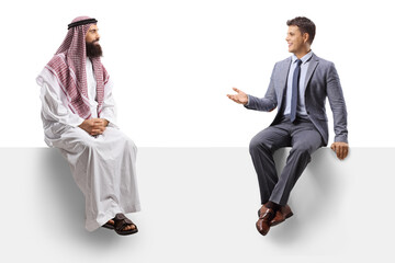 Saudi arab man and a young man in a suit sitting on a blank board and talking
