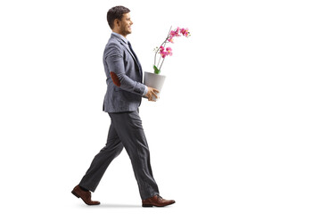 Full length profile shot of a young smiling man in a suit walking a carrying an orchid flower pot