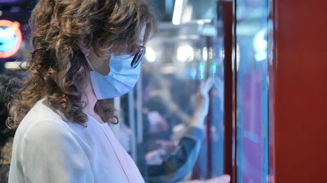 Woman with brown hair wearing protective facial mask and gloves taps on screen choosing items in cafe closeup slow motion