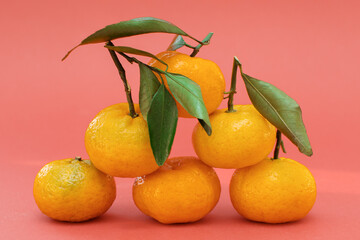 bright, tasty, fresh tangerines with green leaves are stacked in a stack, a pyramid on a red background. Six tangerines. Horizontal photo, close-up.