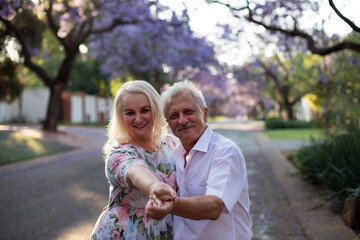 elderly man and woman walk down the street with blooming trees