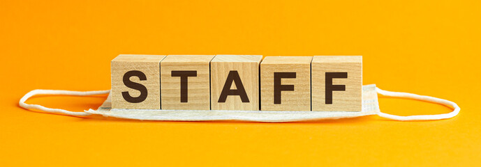 staff the word is written on wooden cubes lying on a medical mask. Concept. yellow background