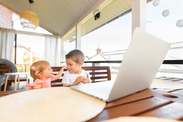 Obraz premium Small smiling kids brother and sister laugh and play laptop, communicate video conference chatting. Spacious cozy home interior.
