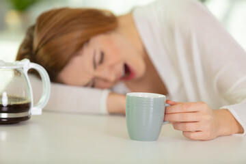 tired woman sleeping on the kitchen table drinking coffee