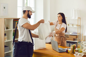 Young food delivery guy taking bags with packed lunch from takeaway cafe worker