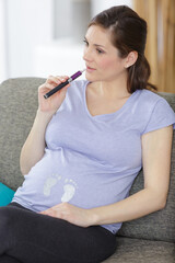 happy pregnant vaping woman sitting on sofa at home