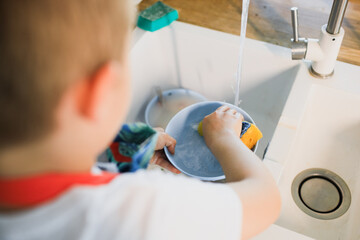 a little boy washes dishes in a modern kitchen.