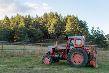 Obraz premium Old red tractor next to ranch in autumn on a sunny day