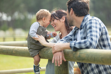 parents with their toddler sat on fence in the countryside