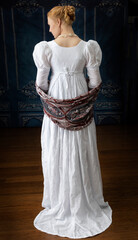 A Regency woman wearing a white muslin dress standing alone in a room