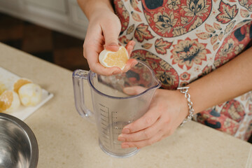 A photo from above of the hands of a woman who is crushing lemon juice by the hand into the blender cup in the kitchen.