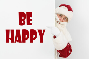 Santa Claus points his fingers at the board with the text - BE HAPPY