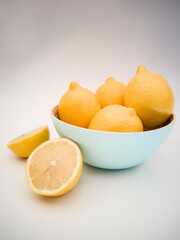 Light blue bowl with yellow lemons inside and a lemon cut in half on the white background. Juicy, fresh and colorful fruits on white background