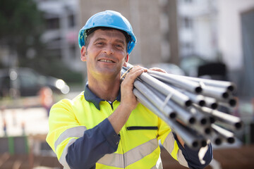 worker carrying pipes on his shoulder on construction site