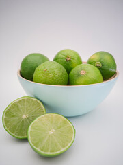 Light blue bowl with green limes and one lime outside cut in half on white background. Juicy colorful fruits for mojito. Freshness and health.