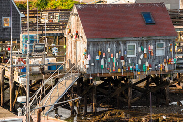 Fototapeta na wymiar Wooden fishing hut wiht hanging colourful buoys at the end of pier in a fishing harbour at sunset. Kittery, ME, USA.