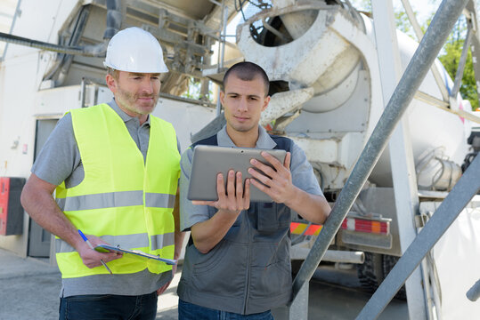 two male workers looking at tablet next to cement lorry
