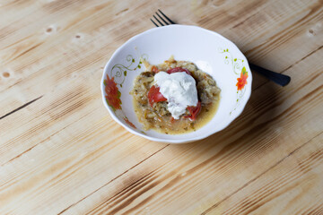Stuffed stewed paprika with sour cream in white bowl on wooden background