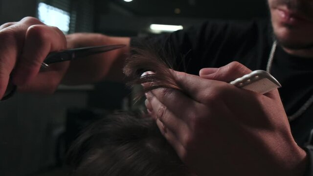 A Barber cuts the hair of a male client in a barbershop. Creating a fashionable men's hairstyle.