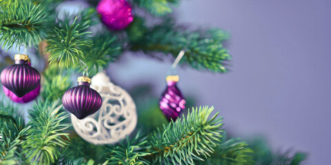 Obraz na płótnie Canvas Banner with beautiful purple glass tree bauble with decorated Christmas tree with other seasonal tree ornaments on light violet background
