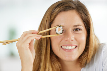 smiling young woman holding sushi with chopsticks