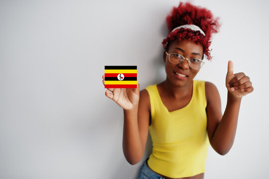 African woman with afro hair, wear yellow singlet and eyeglasses, hold Uganda flag isolated on white background, show thumb up.