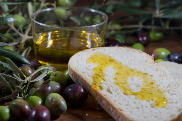 Olive oil in a glass vase with olive branches and olives around on a wooden table