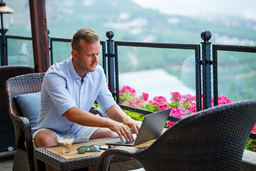 Successful male businessman working on vacation behind a laptop with a mountain view. Online manager workflow. Work outdoors with a beautiful view from the balcony