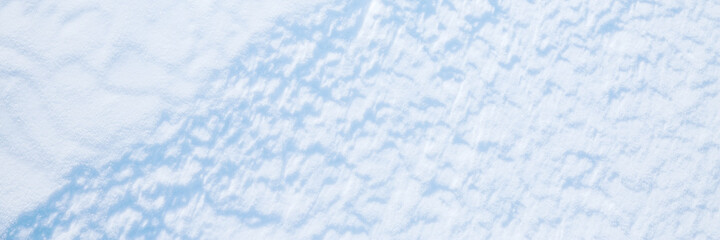Beautiful winter background with snowy ground. Natural snow texture. Wind sculpted patterns on snow surface. Wide panoramic texture for background and design.