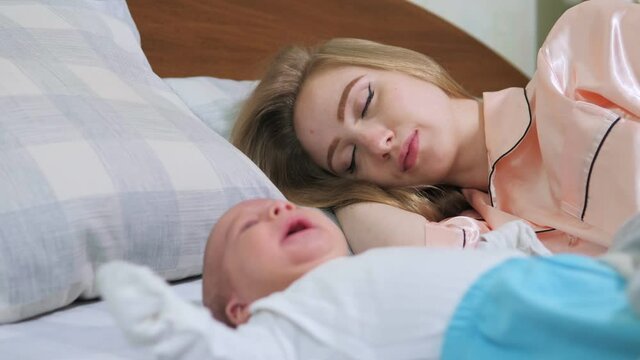 Happy mother and her newborn baby resting in bed together. Maternity concept. Parenthood